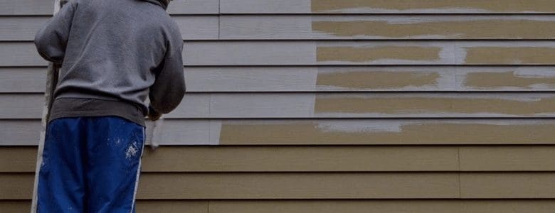 A worker painting the siding, so it is no longer brown, but a light grey color.