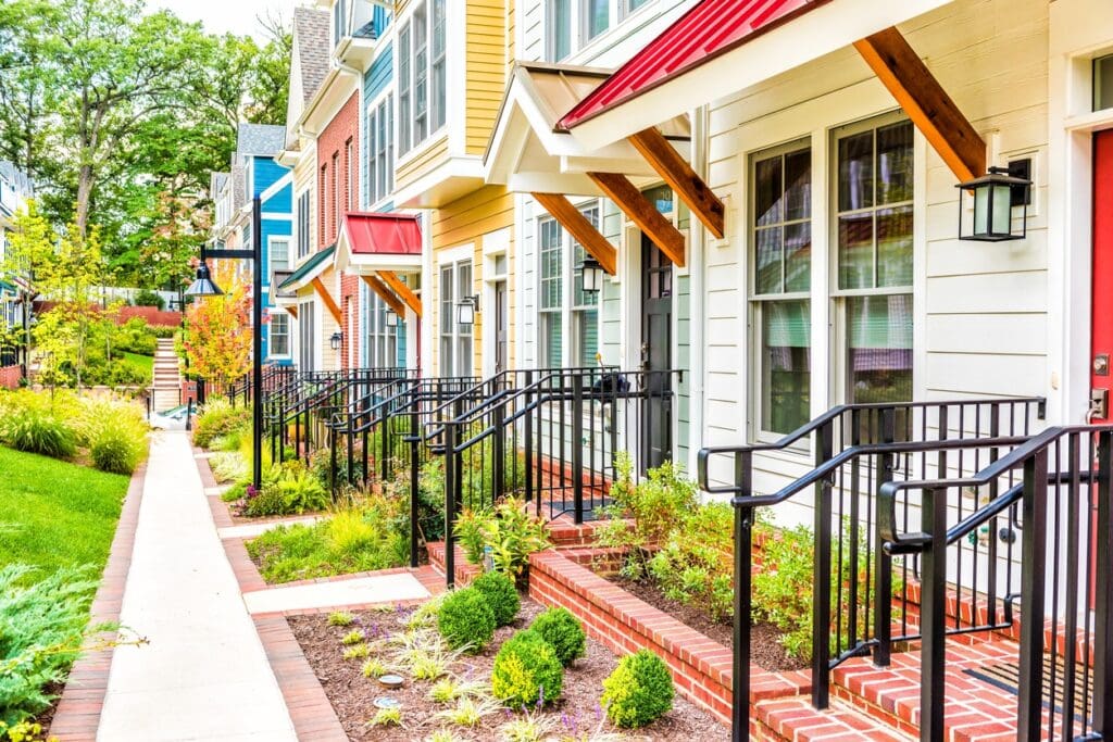 Row of colorful, red, yellow, blue, white, green painted residential townhouses and homes with brick patio gardens in summer