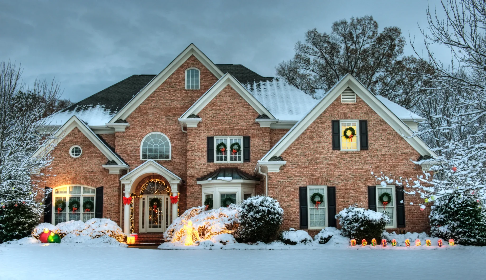 large brick home decorated for holidays with snow