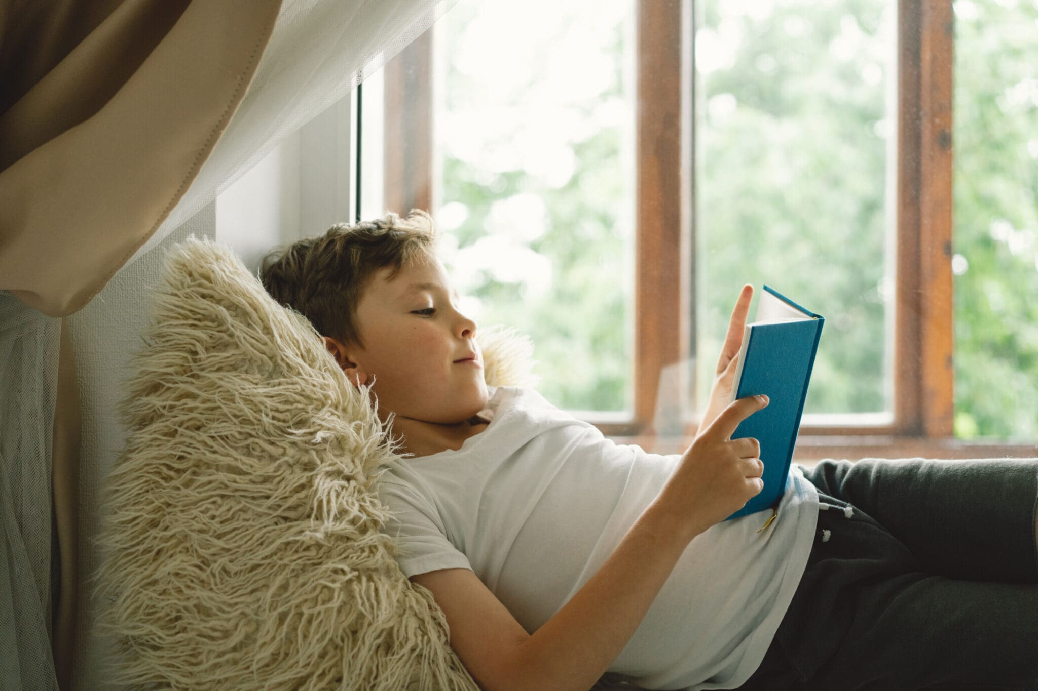 boy reading a book on the windowsill near the window