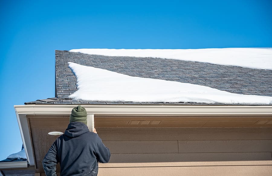 Home contractor checking a residential roof with remaining snow as part of spring roof preparation in New Jersey.